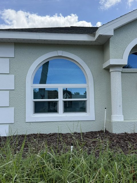 Window replacement in Florida: arched impact window with grids over a double window in a gray stucco wall