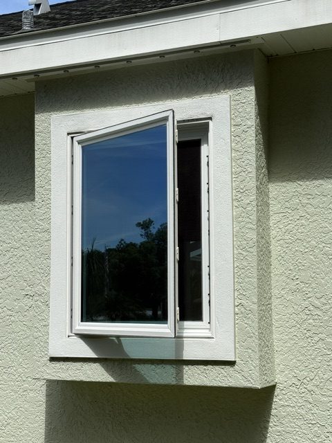 Casement impact window opened on a stucco home