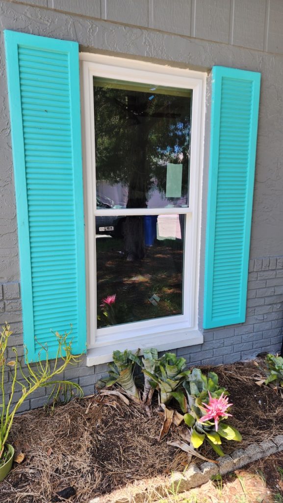 Single hung impact window between teal shutters