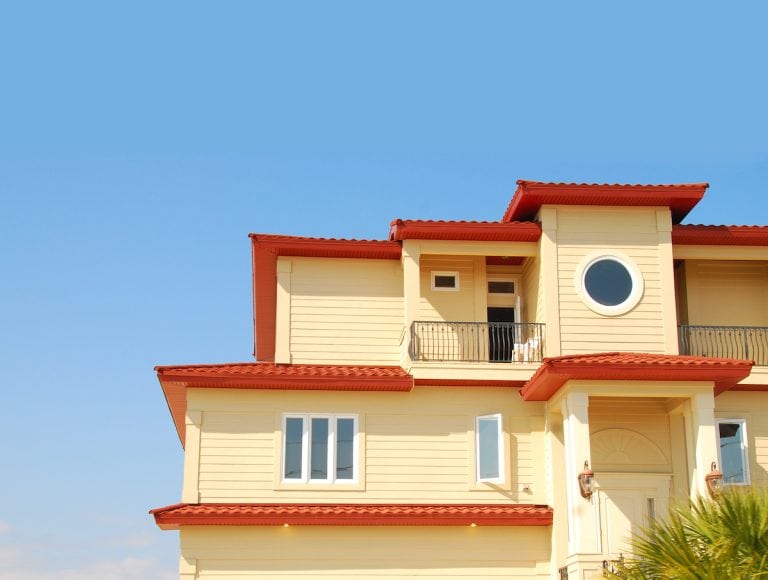 Multilevel coastal home with yellow siding, red roof trim and a balcony