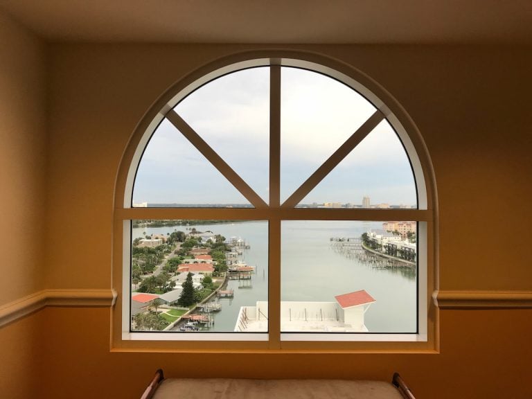 Arched window with grid pattern framing a waterfront view of homes and boats