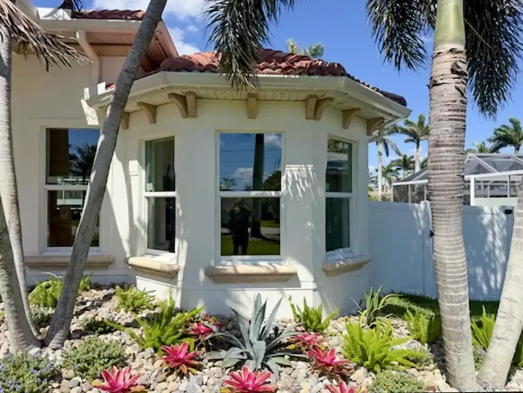 White-framed bay windows beside tropical landscaping