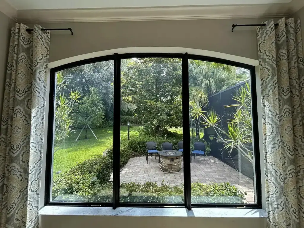 Black-framed arched window group viewed from a room with curtains