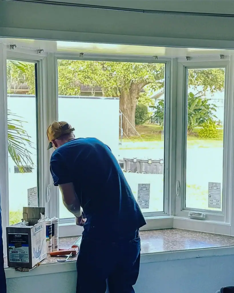 Installer working on a white-framed bay window inside a home