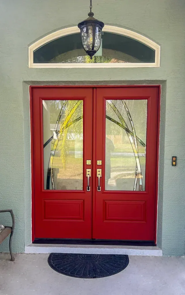 Red double entry doors with glass panels beneath an arched transom