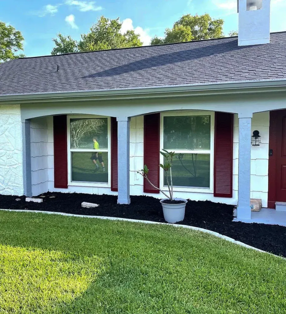 White single-hung windows with red shutters on a landscaped home